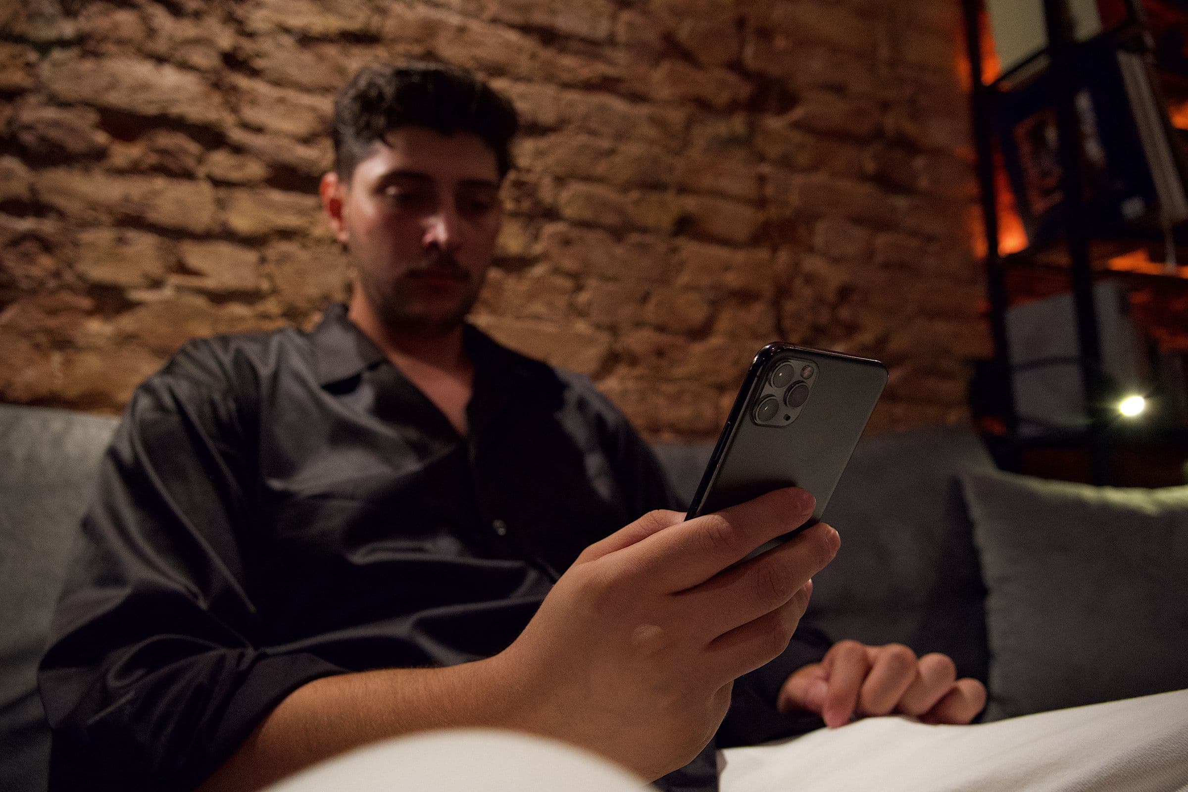 A man relaxing on a couch at night, reading on his phone
