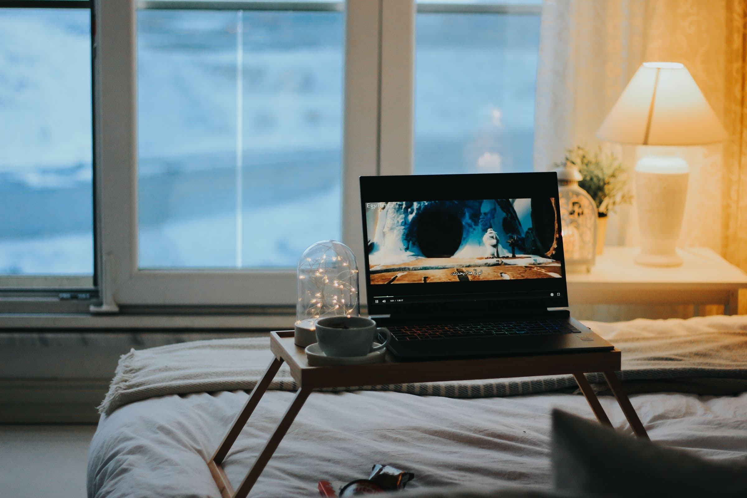A laptop playing a video on a tray table in a bright bedroom